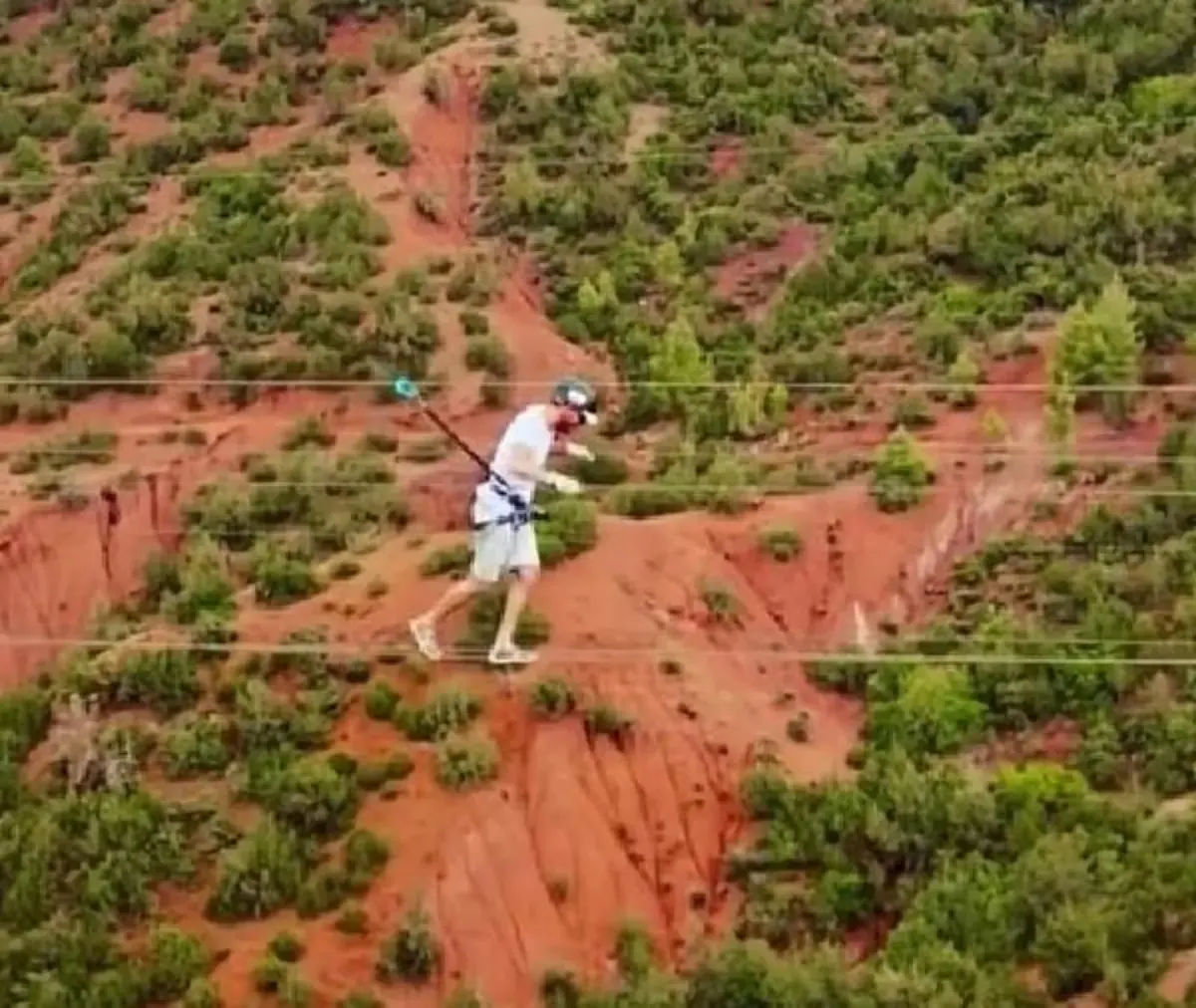 Walker crossing a suspended rope bridge above a red valley