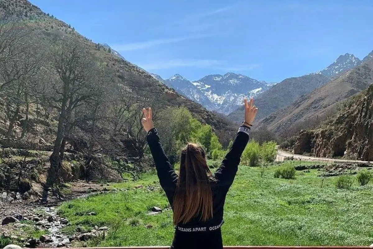 Hiker with raised arms facing snowy Atlas peaks